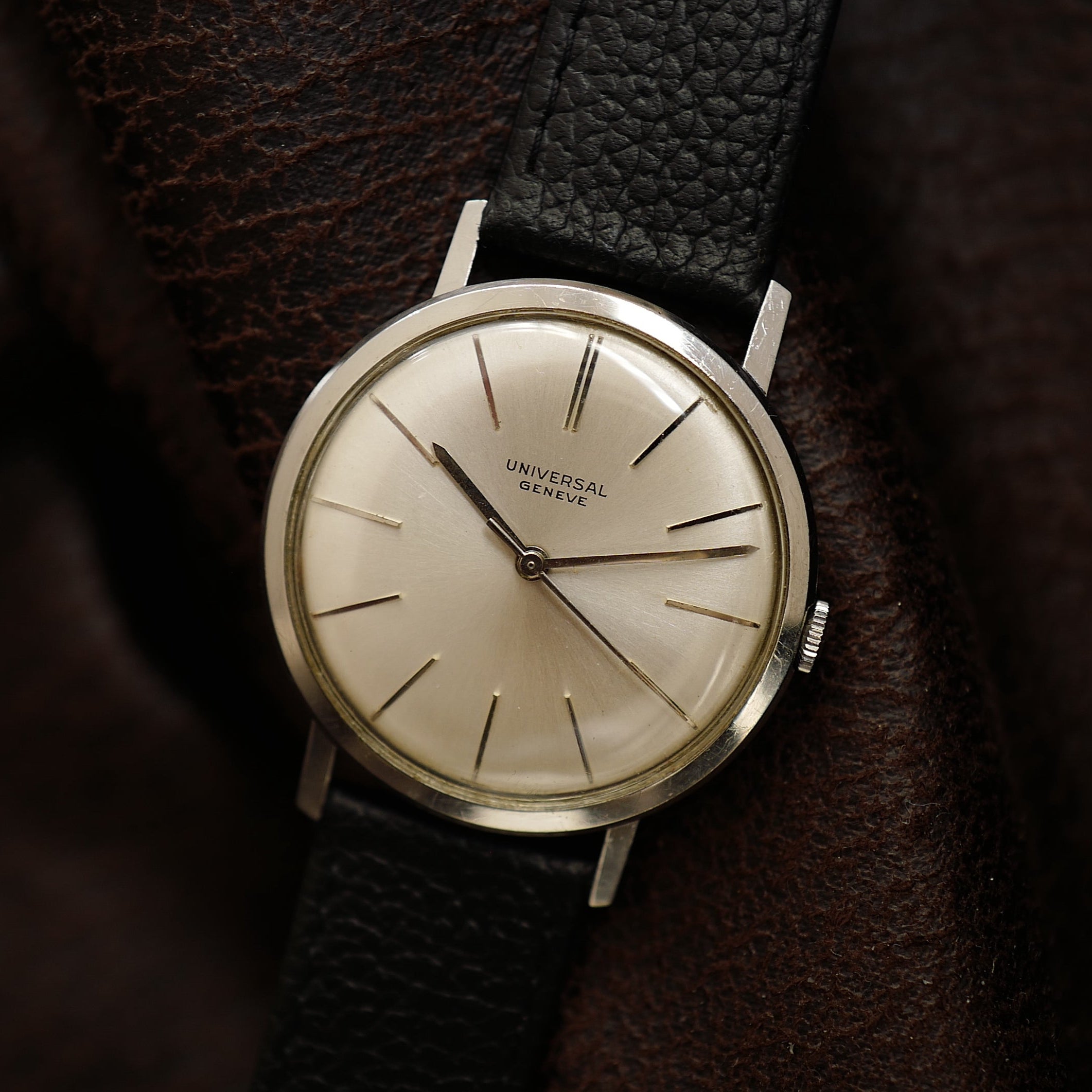 Montre Universal Genève à boîtier fin argenté et cadran vintage des années 1960, vue de face avec bracelet en cuir.