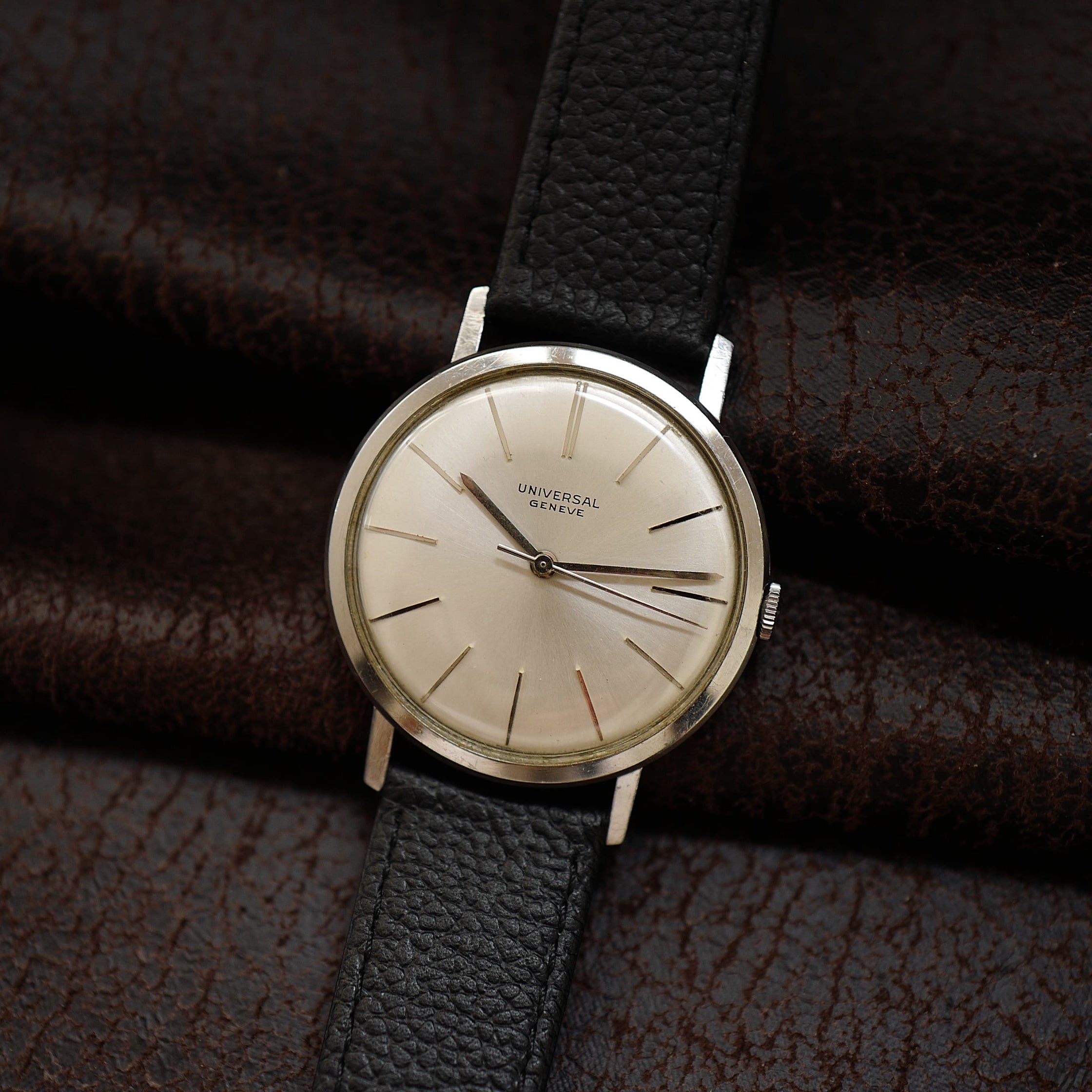 Montre Universal Genève à boîtier fin en argent avec cadran des années 1960, affichant l'heure avec aiguilles et index élégants.