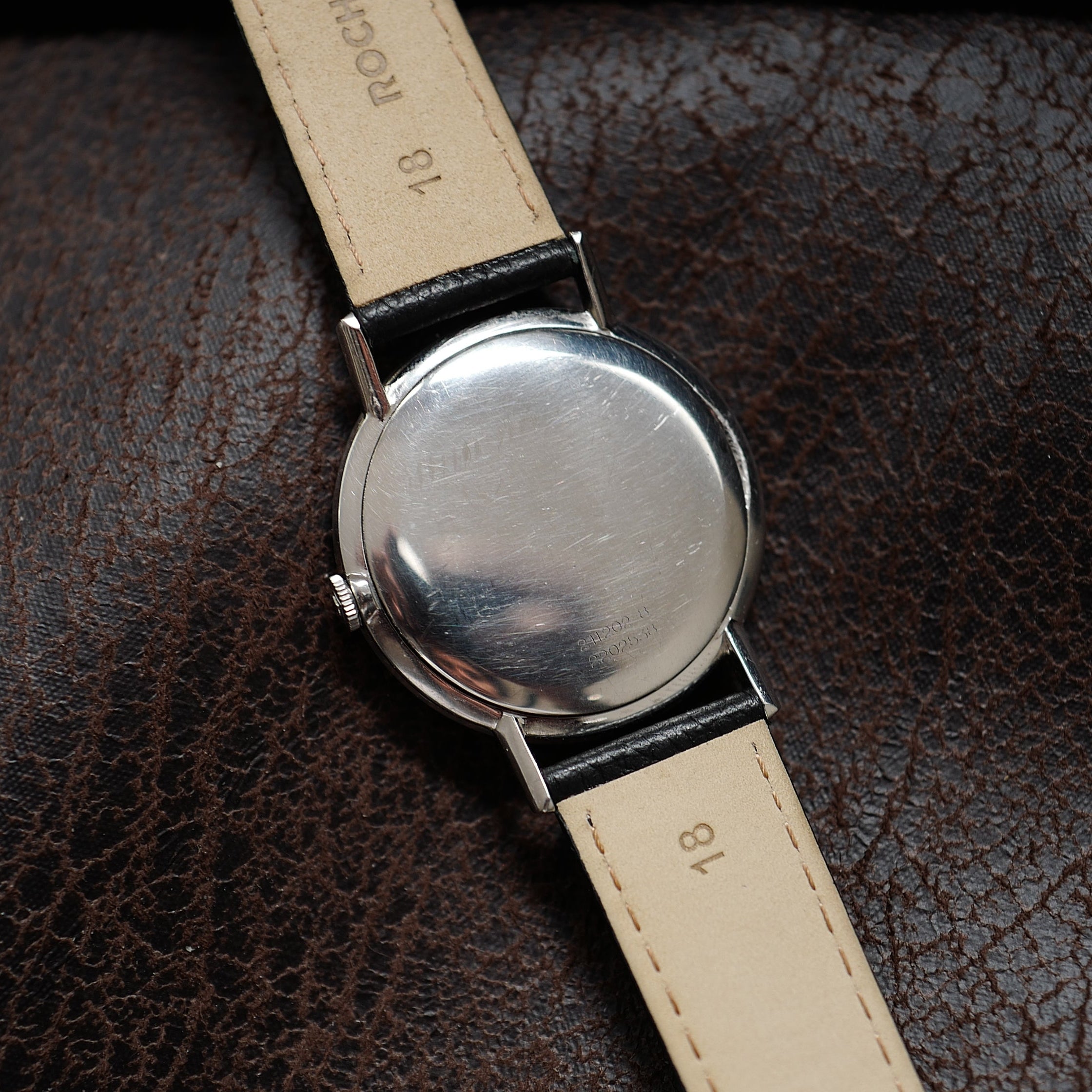 Montre Universal Genève à boîtier mince, cadran argenté, style années 1960, visible avec bracelet en cuir beige.